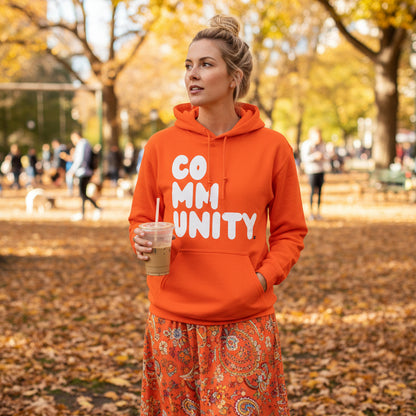 Woman standing in the park wearing the APWT Gift Shop's A Community in Orange Citrus Unisex Hoodie from the Community Collection