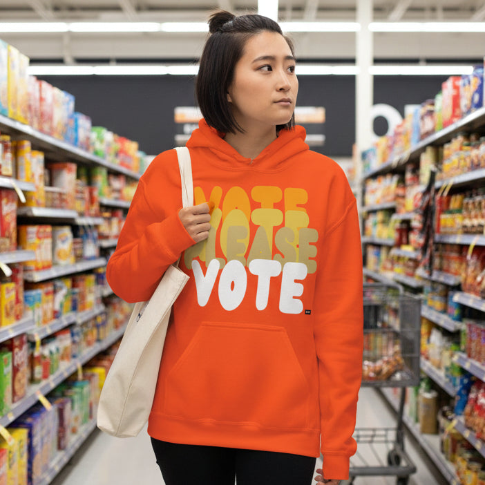 Woman walking through a grocery store wearing the APWT Gift Shop's Please Vote in Safety Cone Orange Unisex Hoodie from the APWT Vote Shop