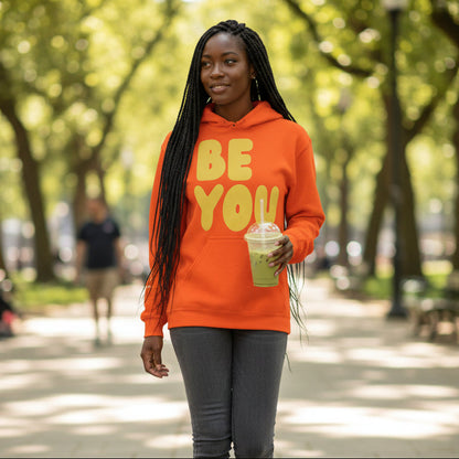 Woman walking through a city park wearing the APWT Gift Shop's Be You in Orange and Yellow Unisex Hoodie from the Be You Collection