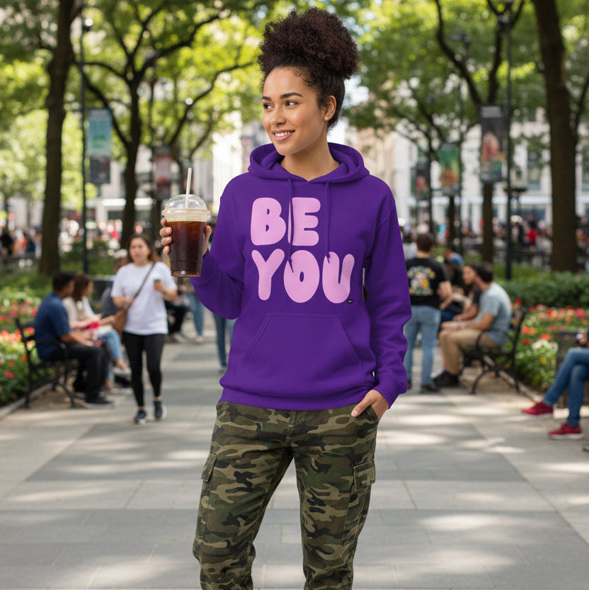 Woman standing in a city park wearing the APWT Gift Shop's Be You in Purple and Pink Unisex Hoodie from the Be You Collection