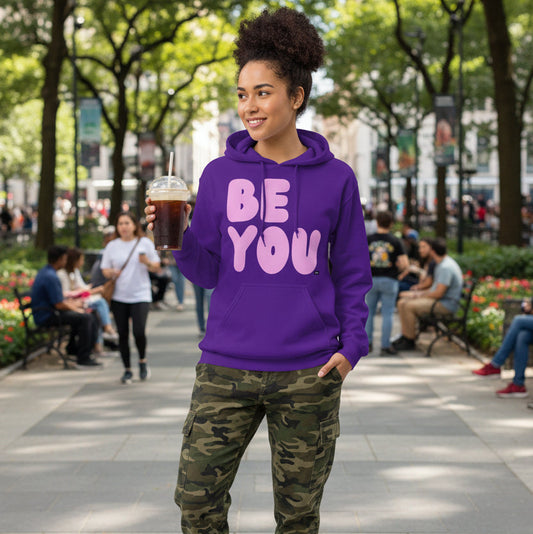 Woman standing in a city park wearing the APWT Gift Shop's Be You in Purple and Pink Unisex Hoodie from the Be You Collection