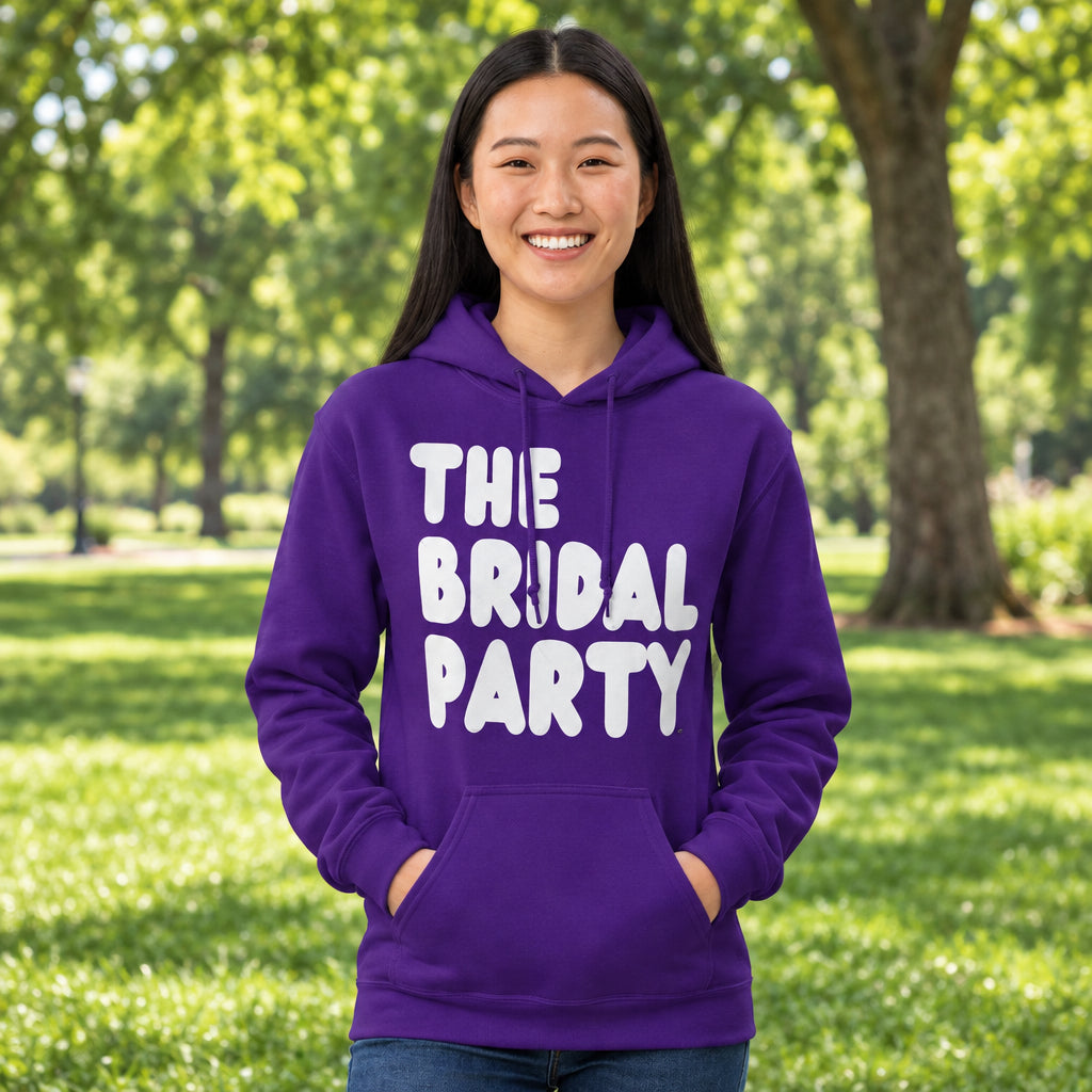 Woman standing in a park wearing the APWT Gift Shop's The Bridal Party Unisex Hoodie from the APWT Wedding Shop in Purple