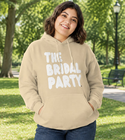 Woman standing in a park wearing the APWT Gift Shop's The Bridal Party Unisex Hoodie from the APWT Wedding Shop in Beige