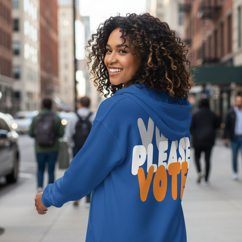Woman walking down the street wearing the APWT Gift Shop's Please Vote in Blue and Orange Unisex Zip-Up Hoodie from the APWT Vote Shop