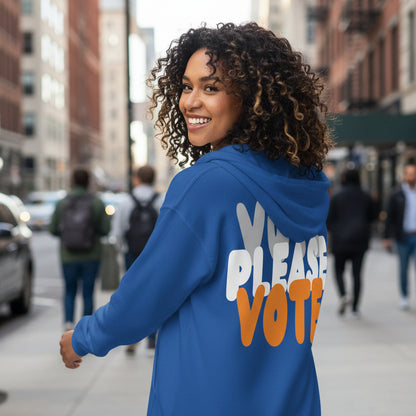 Woman walking down the street wearing the APWT Gift Shop's Please Vote in Blue and Orange Unisex Zip-Up Hoodie from the APWT Vote Shop