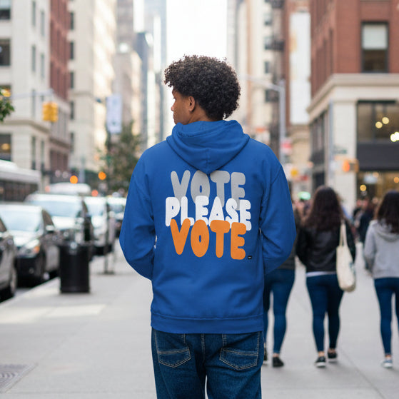 Man walking down the street wearing the APWT Gift Shop's Please Vote in Blue and Orange Unisex Zip-Up Hoodie from the APWT Vote Shop