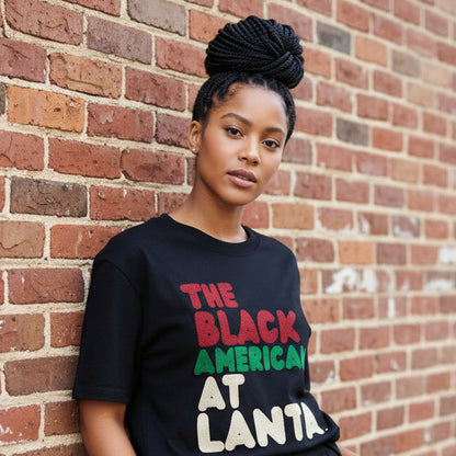 Woman standing against a brick wall wearing the APWT Gift Shop's the Black American Atlanta Premium Unisex T-Shirt from the Black Collection