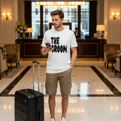 Man standing in a hotel lobby wearing the Groom Premium White T-Shirt from the APWT Wedding Shop