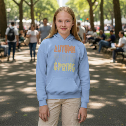 Girl standing in a city park wearing the Fall into Autumn Kid's Unisex Hoodie in Light Blue from the APWT Kid's Shop