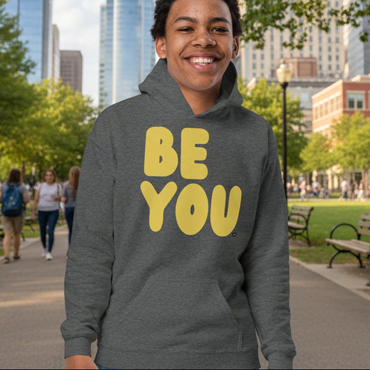 Teen Boy in park wearing Be You Kids in Yellow Unisex Hoodie in Dark Grey from the APWT Gift Shop -  Kids Affirmation Sweatshirts