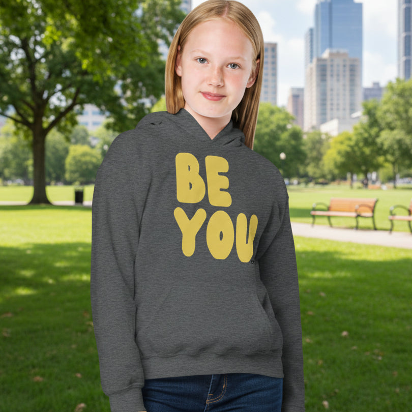 Girl in Park wearing Be You Kids in Yellow Unisex Hoodie in Dark Grey from the APWT Gift Shop -  Kids Affirmation Sweatshirts