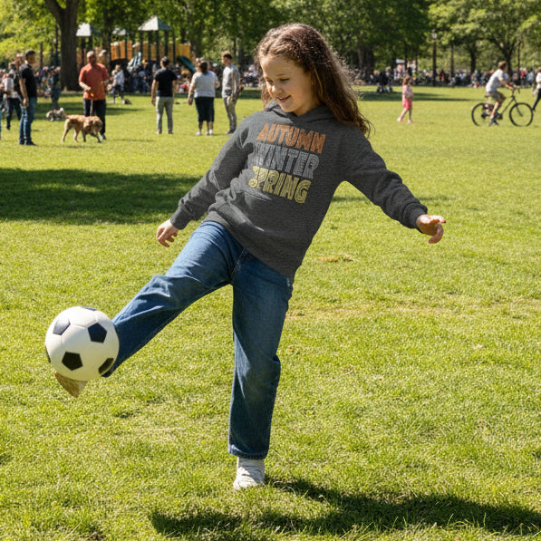 Girl playing soccer in a city park wearing the Fall into Autumn Kid's Unisex Hoodie in Dark Grey from the APWT Kid's Shop