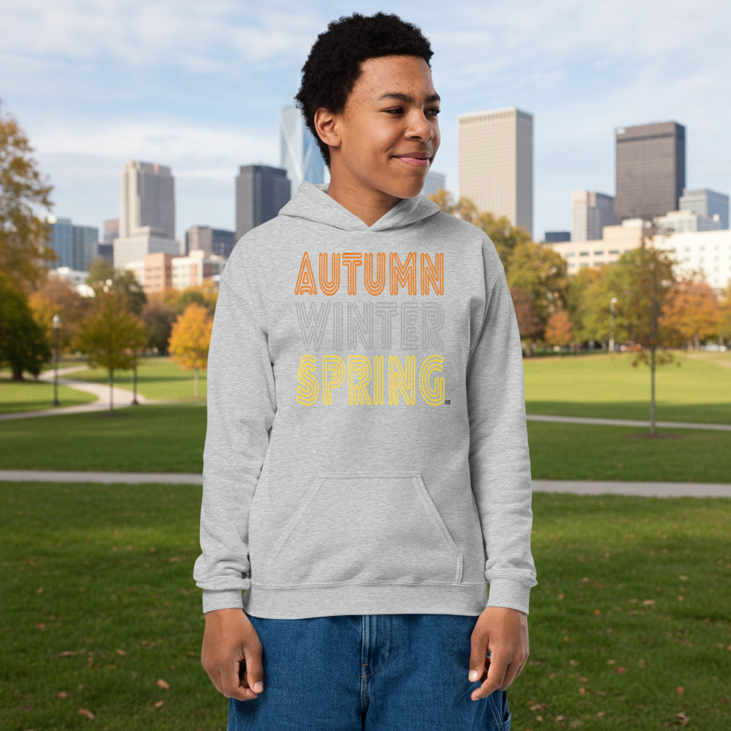 Boy standing in a city park wearing the Fall into Autumn Kid's Unisex Hoodie in Grey from the APWT Kid's Shop