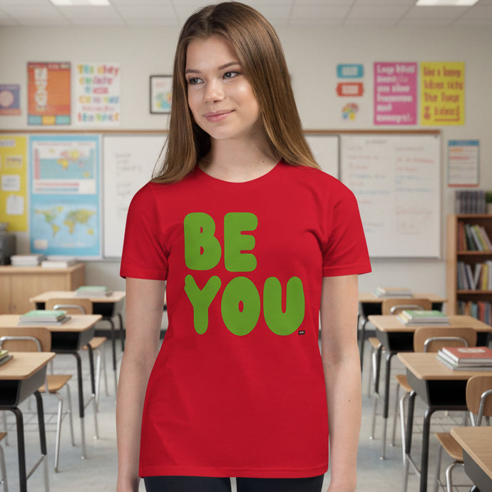 Teen wearing a red t-shirt with 'BE YOU' in green text in a classroom setting