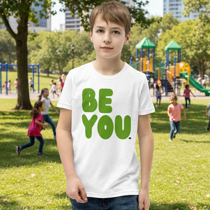 Child wearing a white t-shirt with 'BE YOU' in green letters at a park.